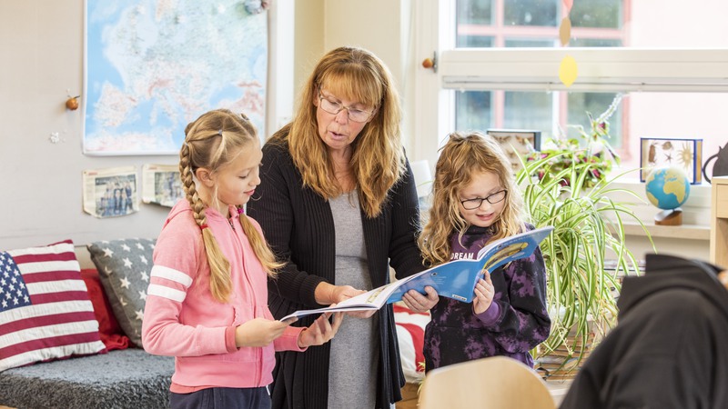 En lärare läser i en bok tillsammans med två barn