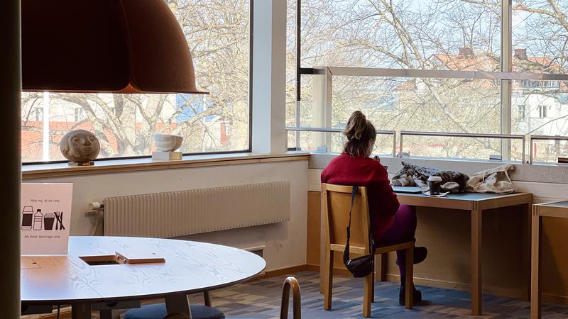 Kvinna som sitter ned vid ett skrivbord på Almedalsbiblioteket i Visby. Hon läser.