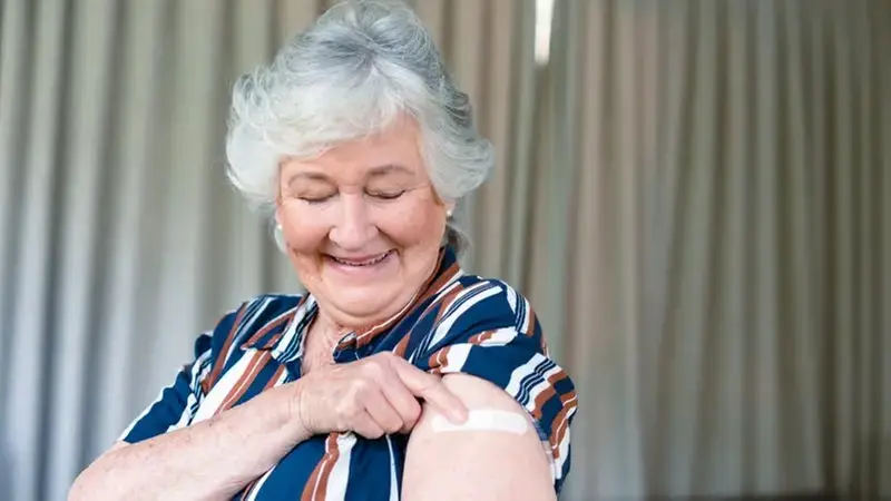 Äldre dam pekar på ett plåster på armen